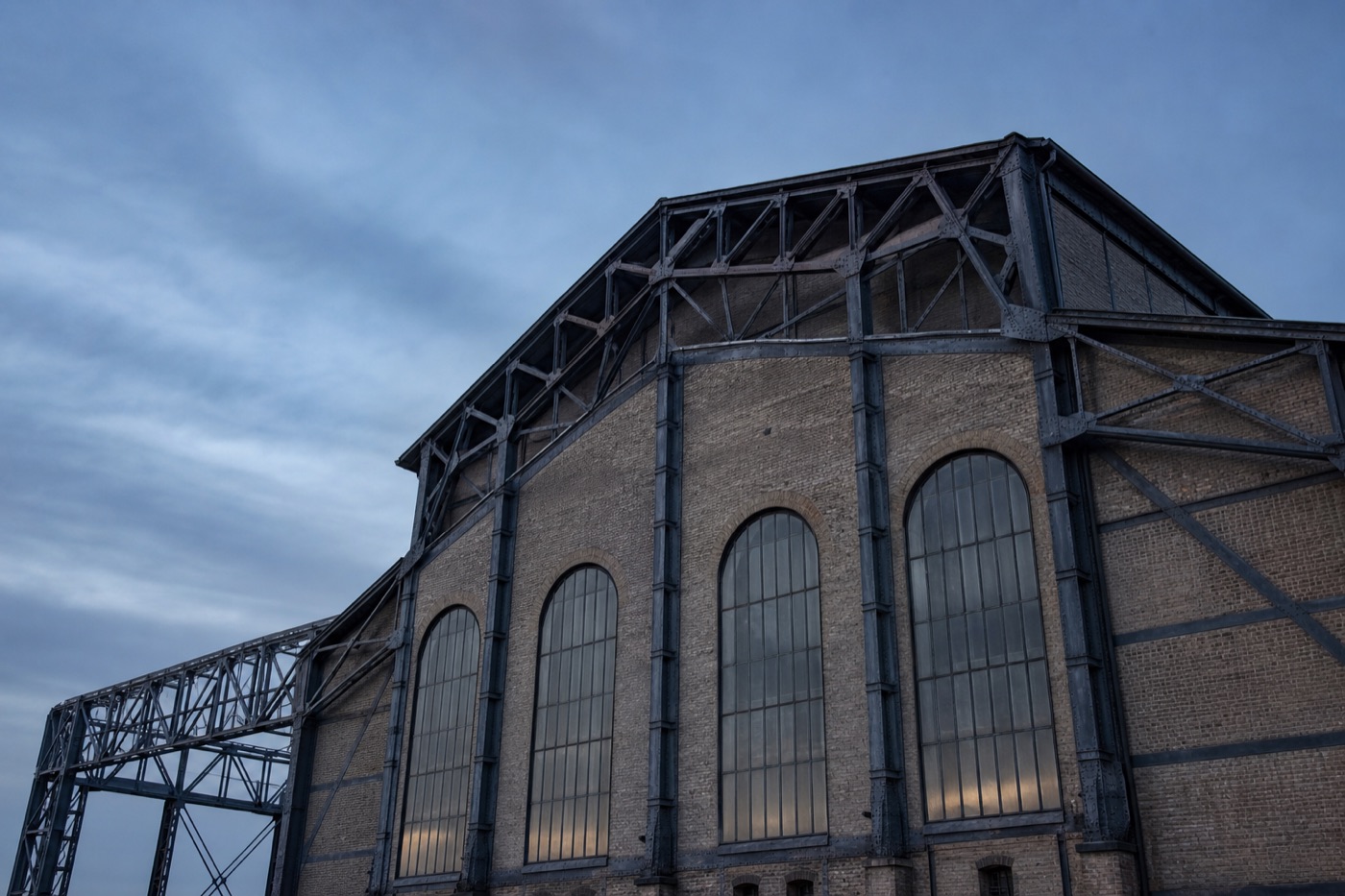 Historische Industriehalle im Ruhrgebiet mit Stahlfachwerk und hohen Bogenfenstern in der Abenddämmerung